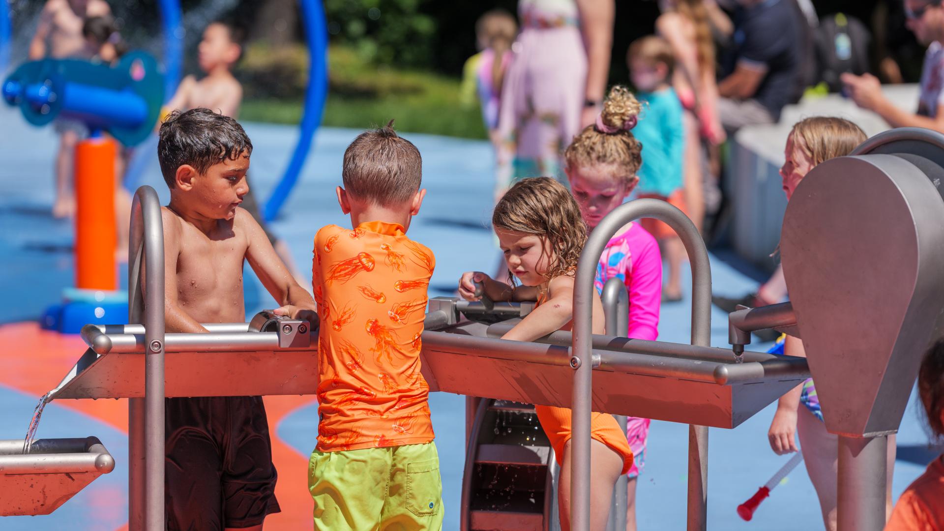 Metal water table with spinning water pump and waterwheel in a spray park and kids playing
